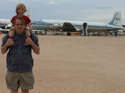 Erika on John's shoulders, in front of an airplane